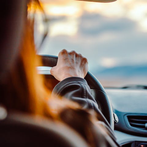 Close-up of a woman's hand on the steering wheel while driving with a scenic view ahead.